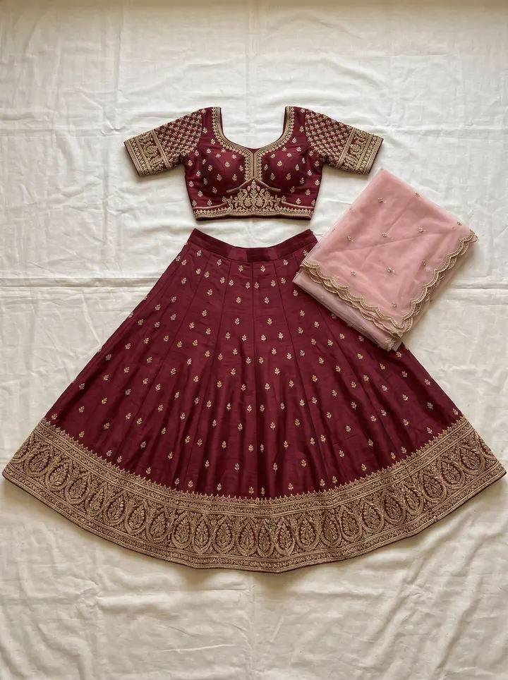 Deep maroon raw silk lehenga, chaude golden zari border ke saath poore gher mein phaila hua, embroidered choli aur pink net dupatta ke saath